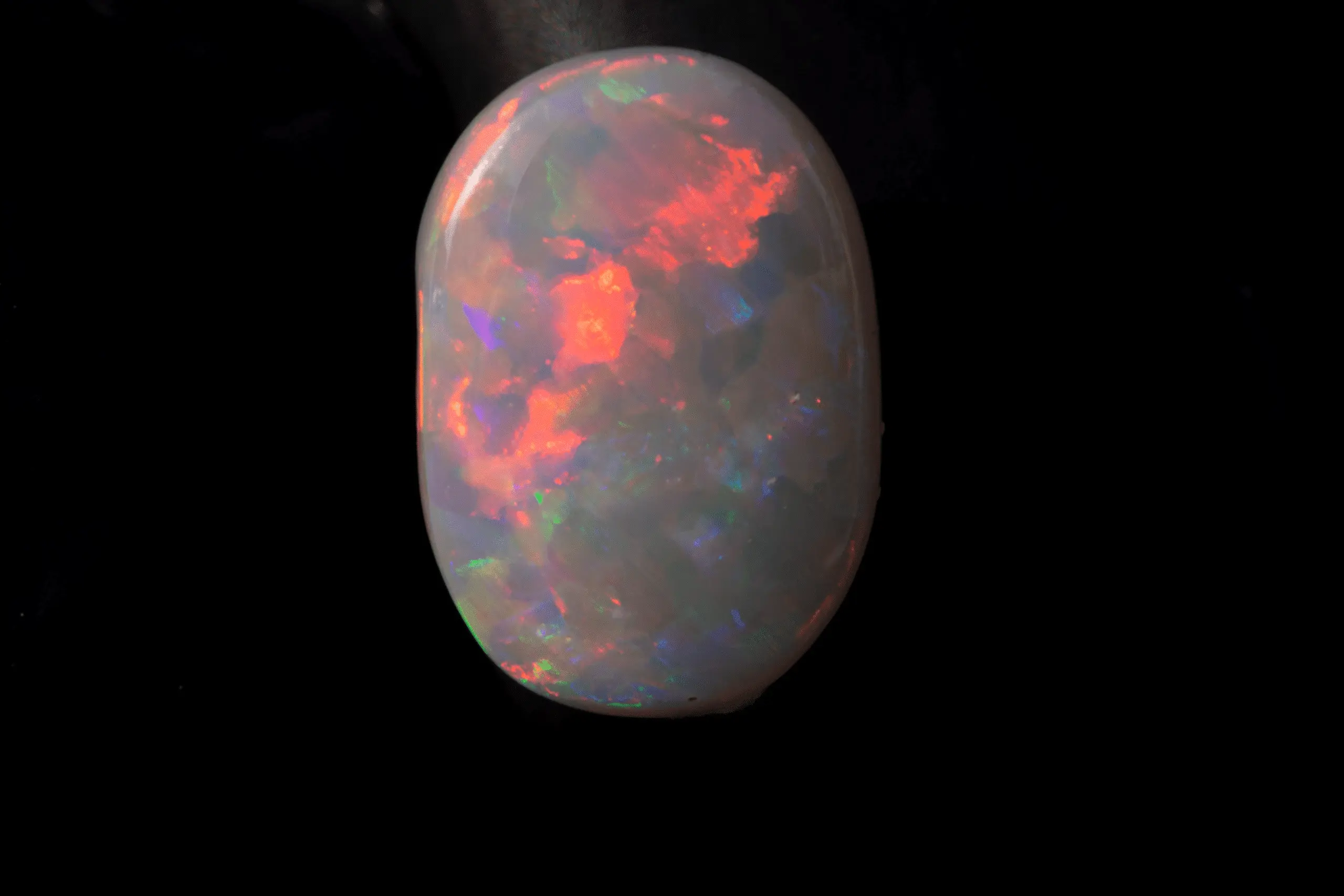 opale naturelle australienne des mines de Coober Pedy, ovale de 0,9 carat d'opale sombre presque de catégorie blanche à brillances multicolores majoritairement rouge et orange
