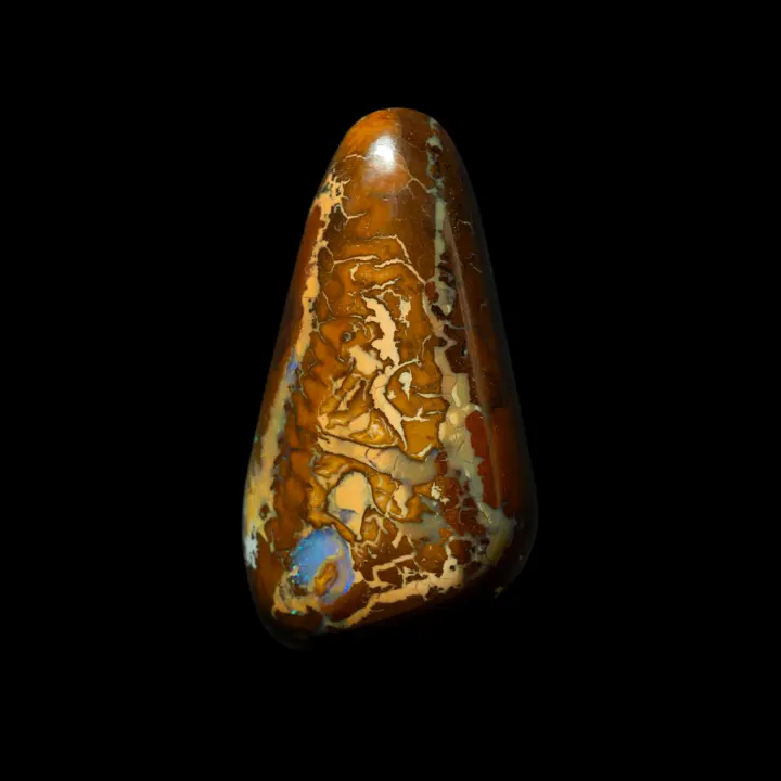 Natural Australian opal from the Koroit mines, free-form near-triangle shape of 26.4 carats with mixed patterns tinged with ochre, yellow, caramel and punctuated by opalized areas with blue brilliance.