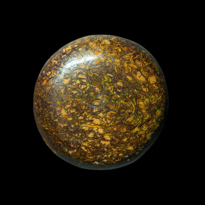 A 48.4-carat circle-cut natural opal from the Koroit mines in Australia, its ochre matrix is crisscrossed with interlacing brights of a deeper yellow and sprinkled with green and violet glints.