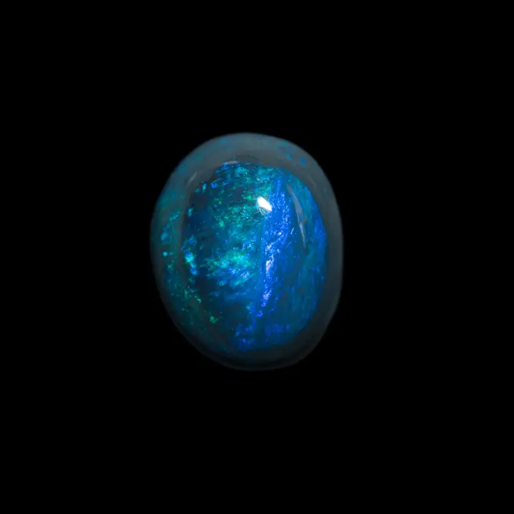Opale naturelle Australienne des mines de Lightning Ridge, cabochon de 2,7 carats d'un bleu intense enlacé d'un anneau gris fumée et ponctué de brillances vertes