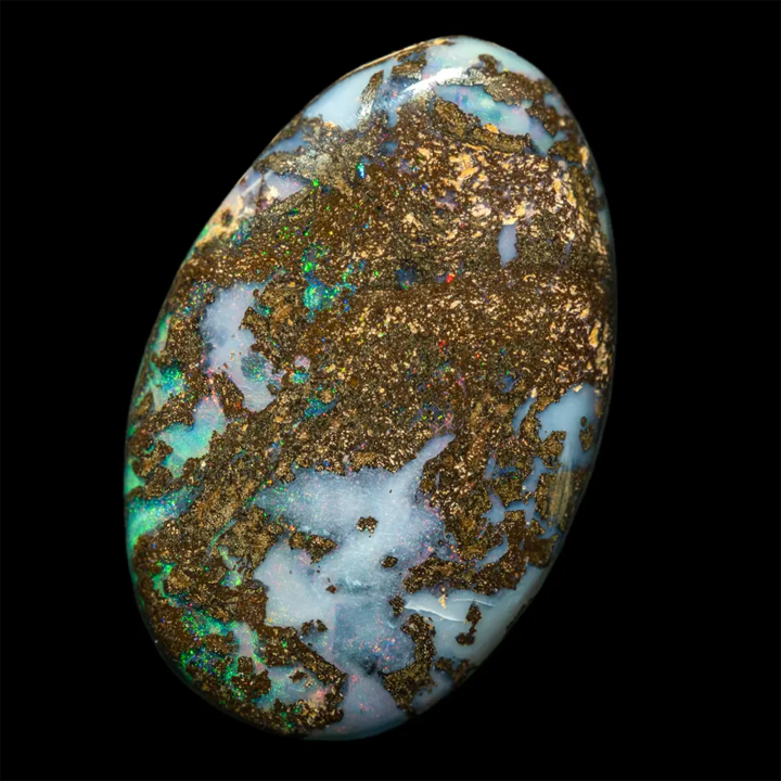 Opale naturelle australienne des mines Koroit. Cabochon elliptique ovale de 13,1 carats à matrice brune micro ponctuée d’ocre jaune clair. L’irisation est brillante sur de nombreuses plages à dominantes vertes ou blanches irisées multicolores