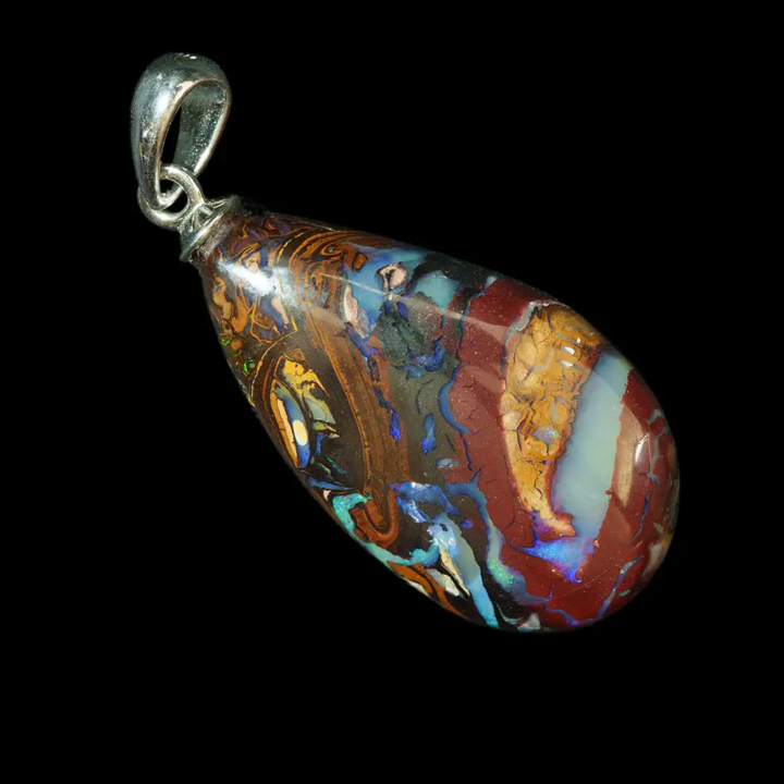 Natural Australian opal from the Koroit mines. An 18.8-carat teardrop-shaped opal set in a 925 sterling silver bail; the rust-ochre and black arabesques highlight the bluish, iridescent bands of the opal’s play-of-color. The contrast between the cool, vivid, iridescent colors and the warm hues of the landscape-like matrix creates an intense, slightly baroque aesthetic for this timeless and unique piece of jewelry.  